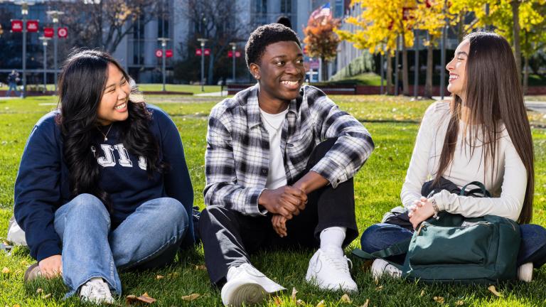 three students sitting on a lawn