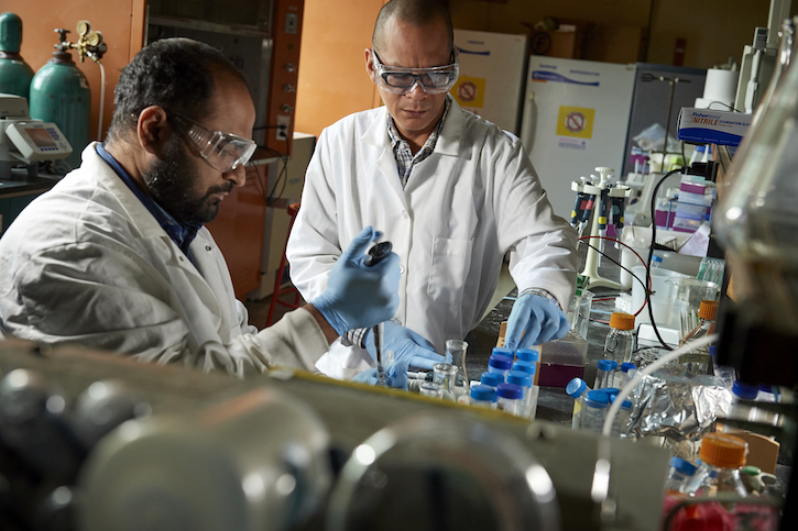 Dr. Edgardo standing next to a chemistry student in a lab doing experiments 