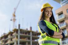 Female engineering intern wearing a safety vest and hard hat in front of a construction site